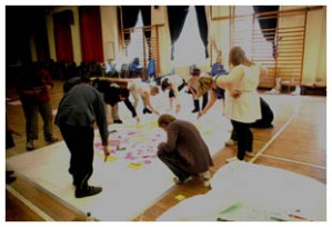 A photo showing the group working on a huge piece of paper on the floor in a hall.